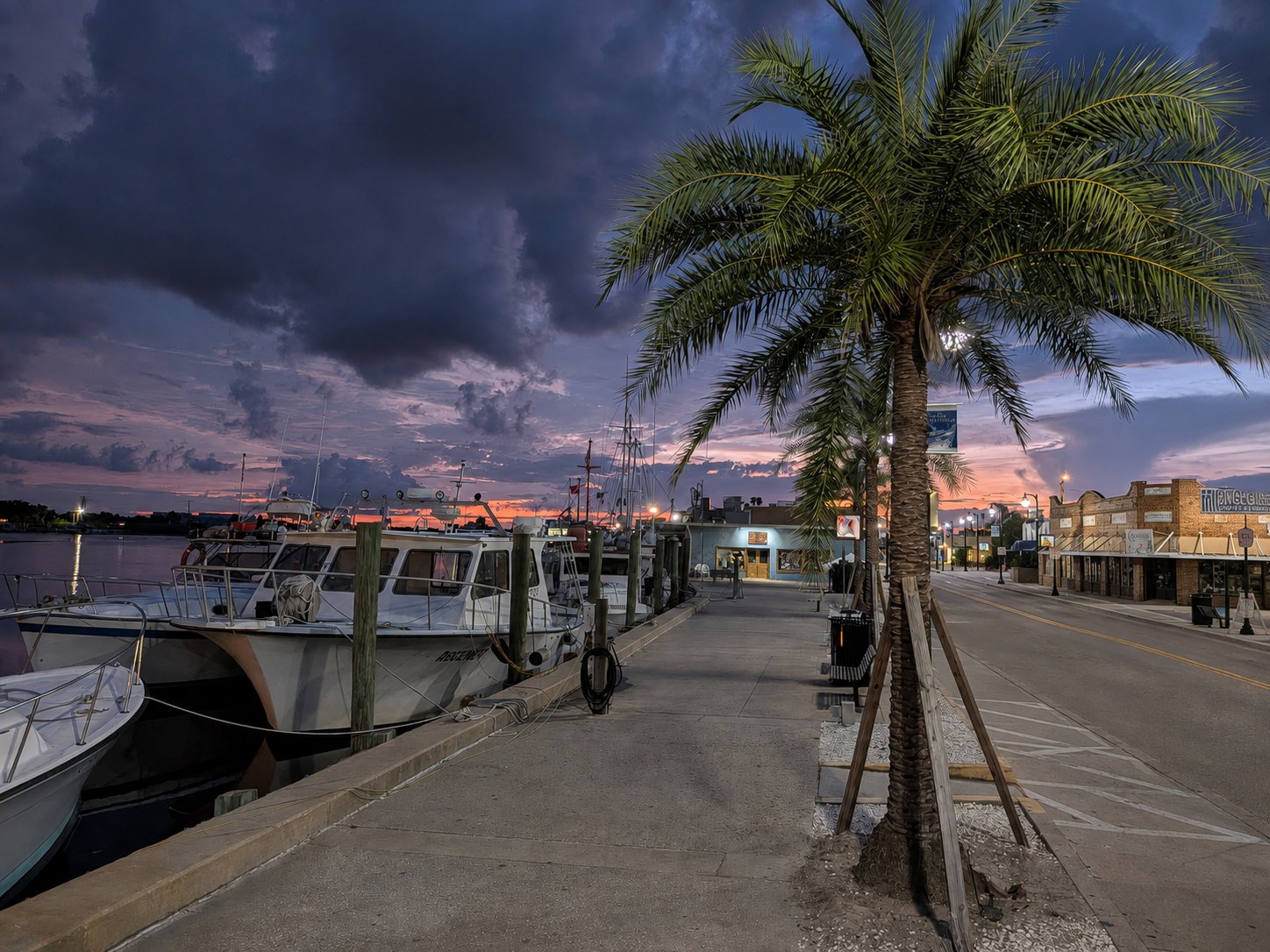The Sponge Docks along the Anclote River before sunrise, with dark clouds above the waterfront and dawn breaking over the water.